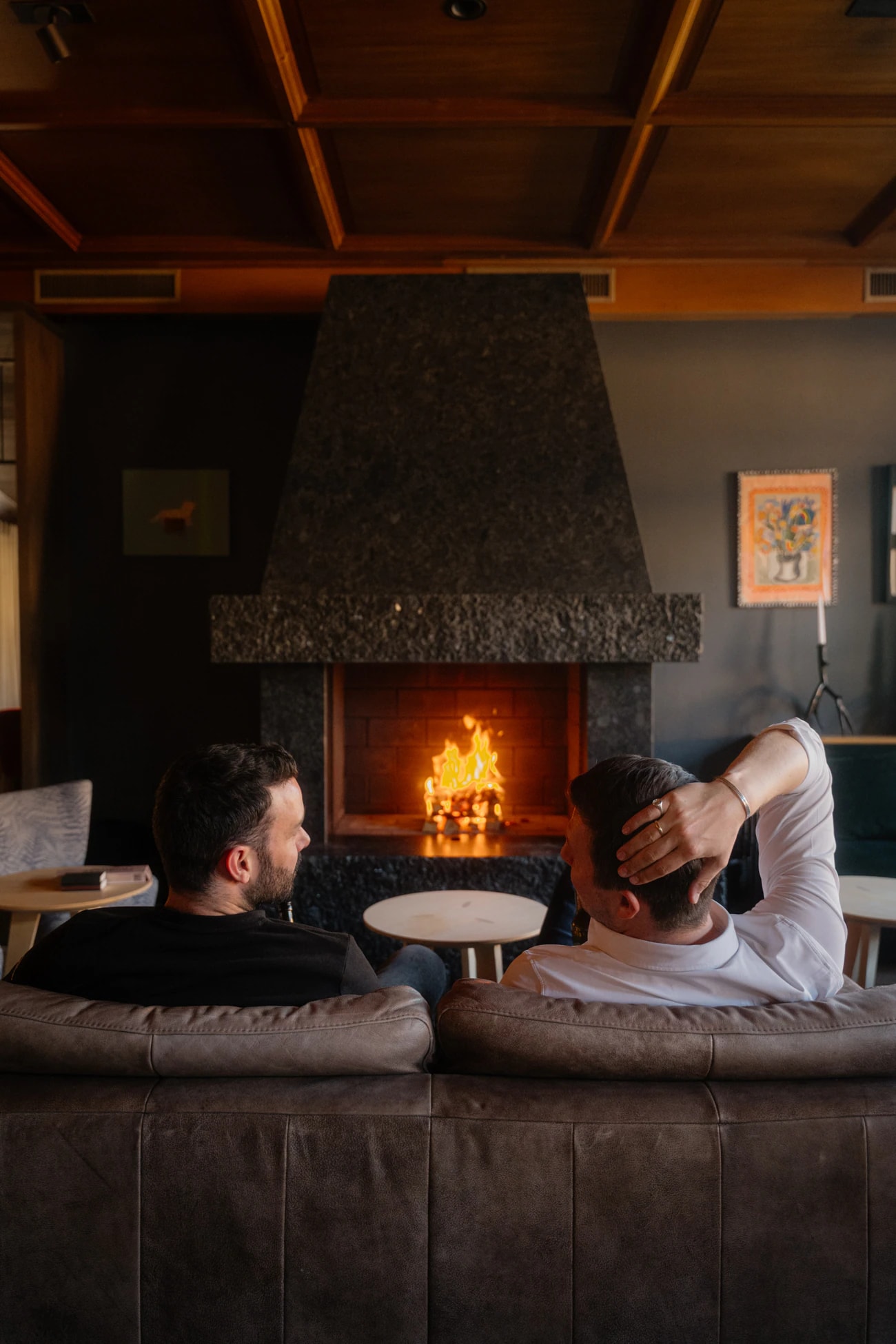 Zwei Gäste auf dem Sofa vor dem neuen Kamin, das Feuer brennt.
