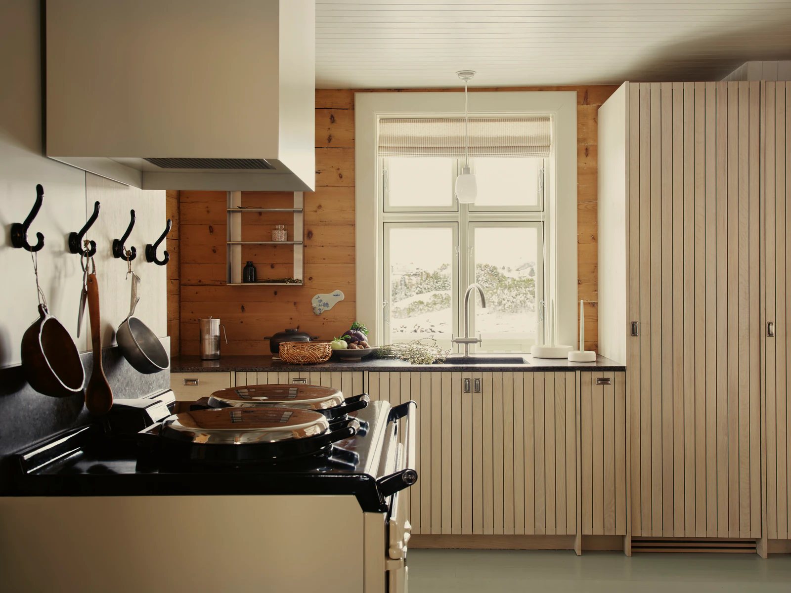 Kitchen with an Aga, pans on hooks and a window onto the snowy island.
