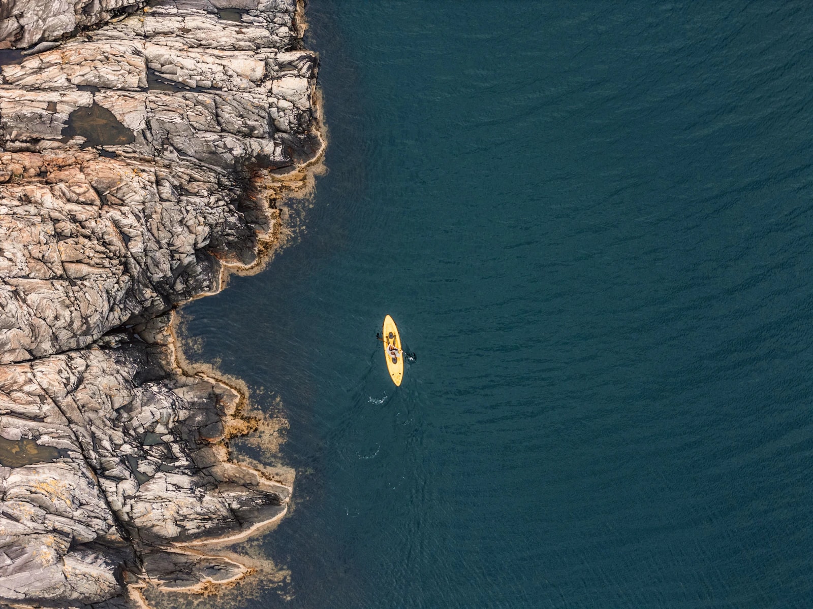 From above: a yellow kayak in deep blue water along the island's rocks.