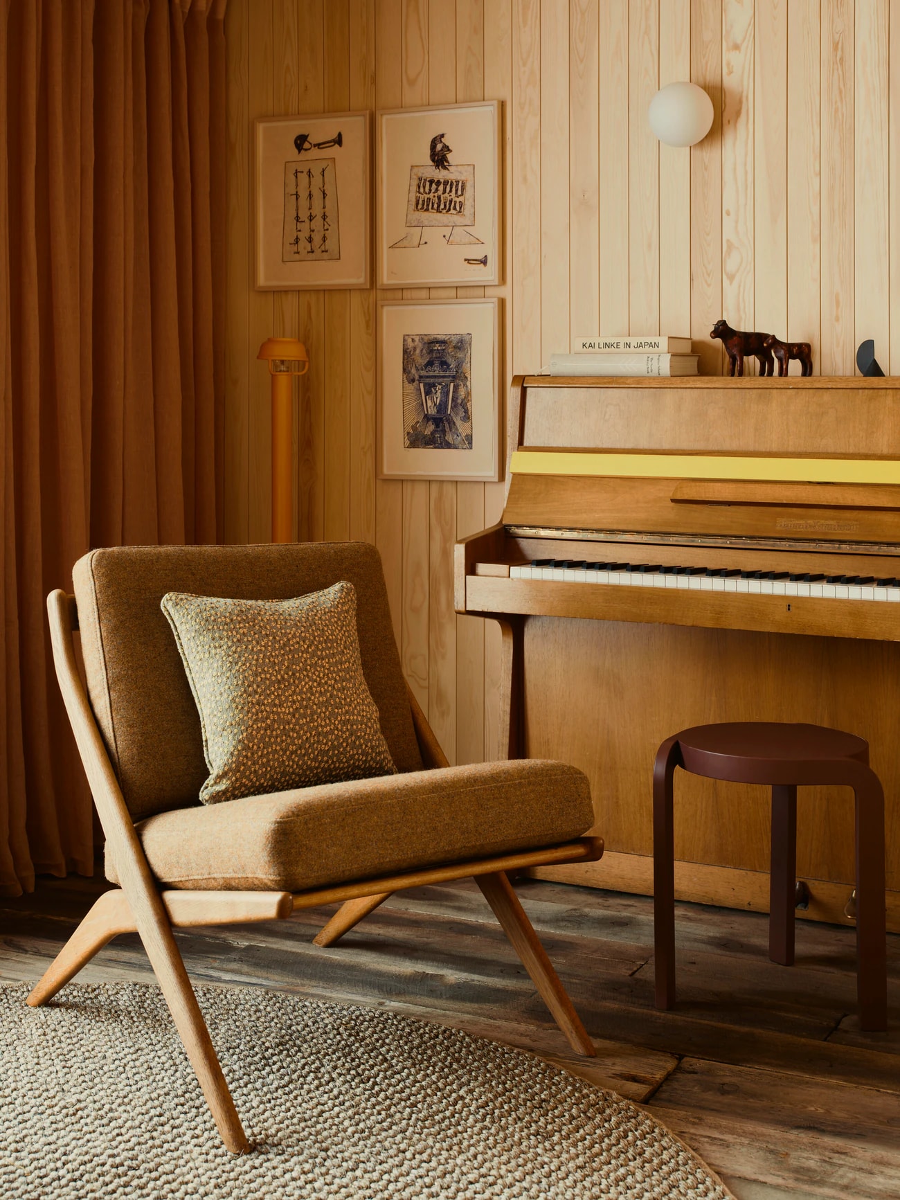 An armchair and a piano in the boathouse, framed drawings on the wooden wall.