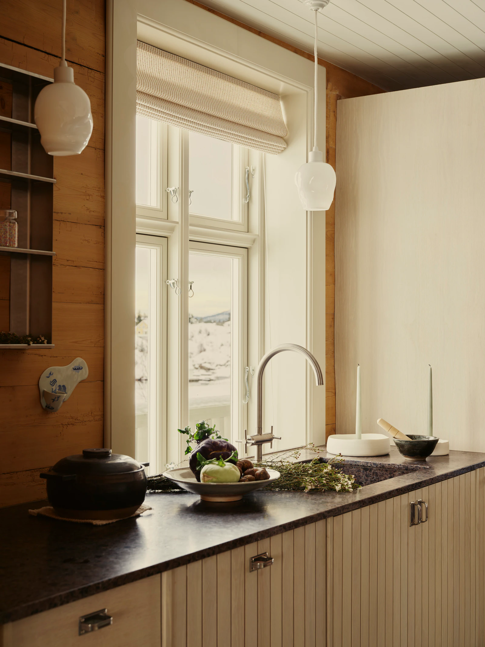 Kitchen counter with a dark worktop beneath the window, a pot, bowls and glass lamps.