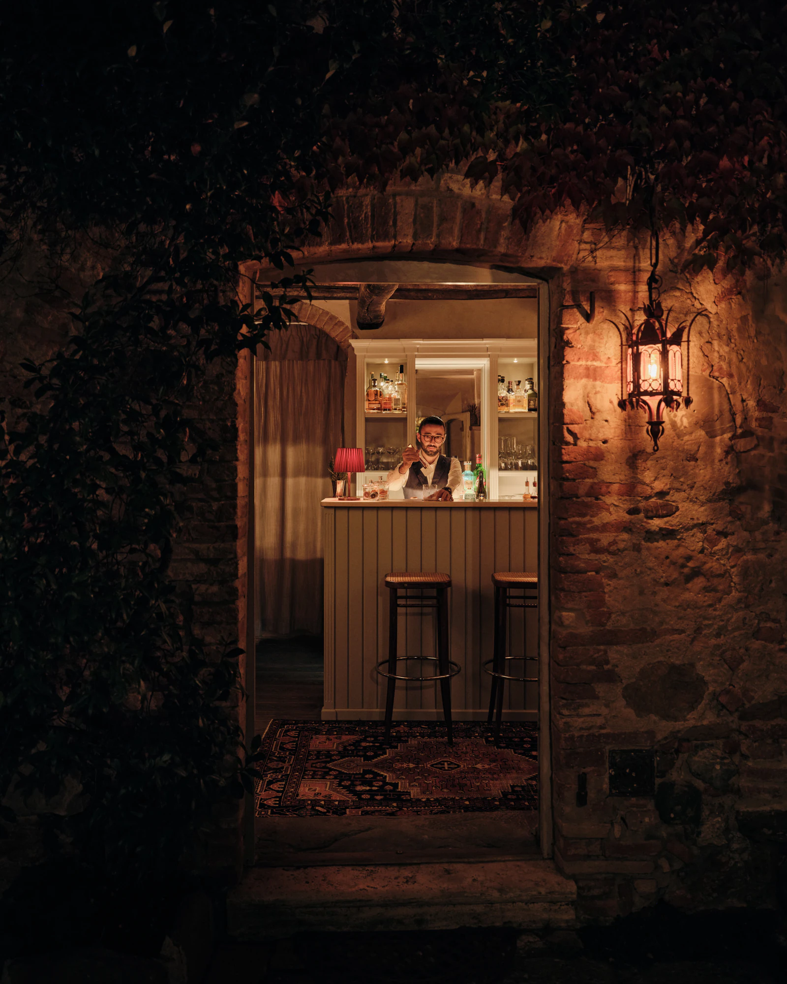 Blick durch eine Steintür in die beleuchtete Bar am Abend.