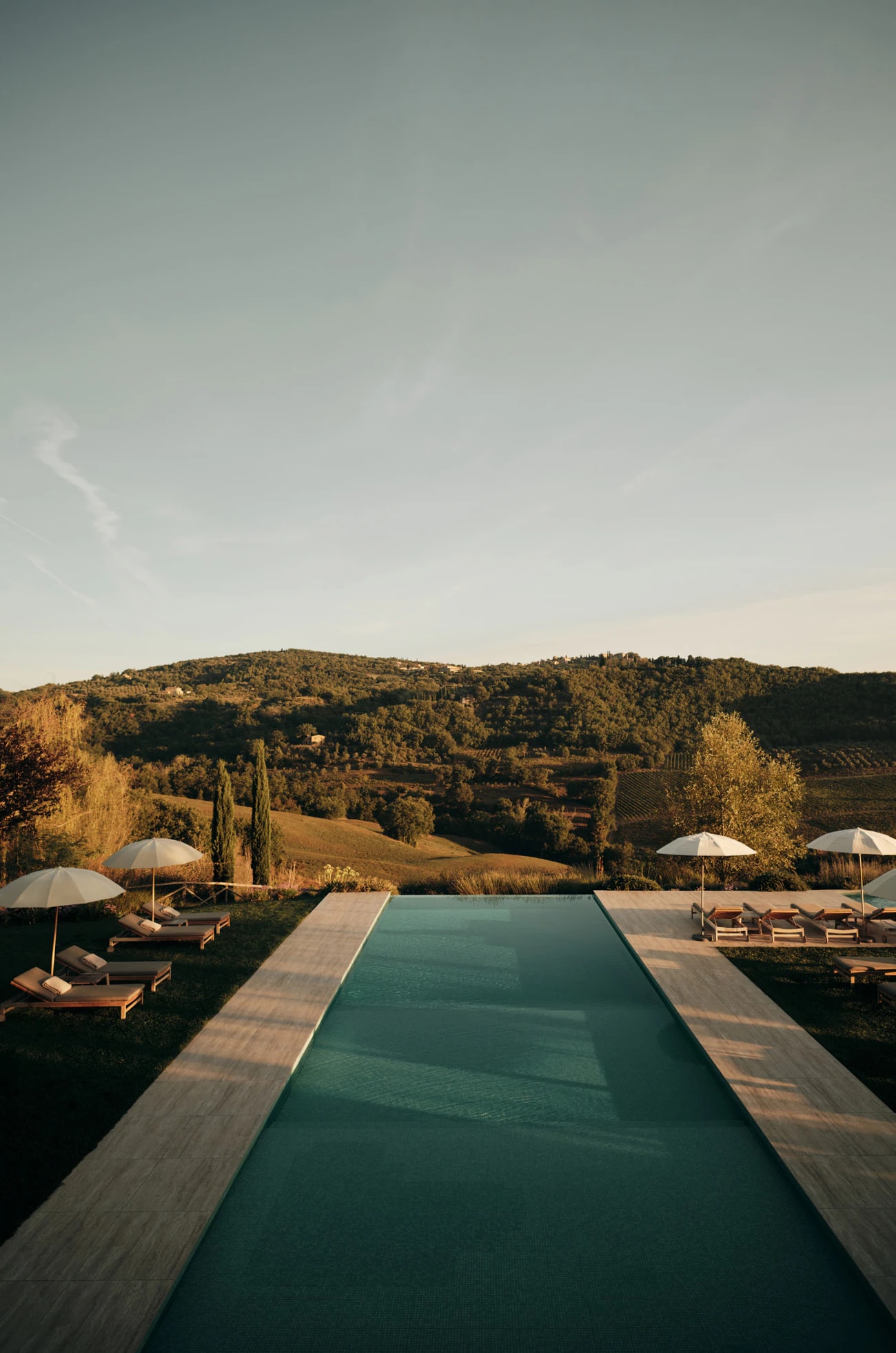 Infinity-Pool mit Sonnenschirmen und Liegen vor den Hügeln im Abendlicht.