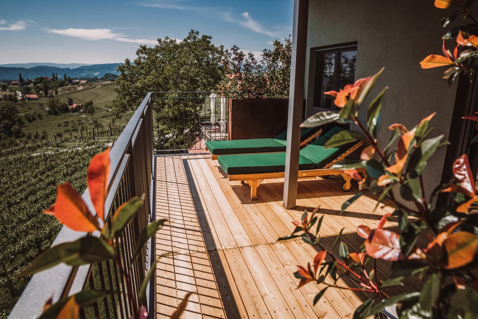Balkon mit Holzboden und Liegen, dahinter Weingärten