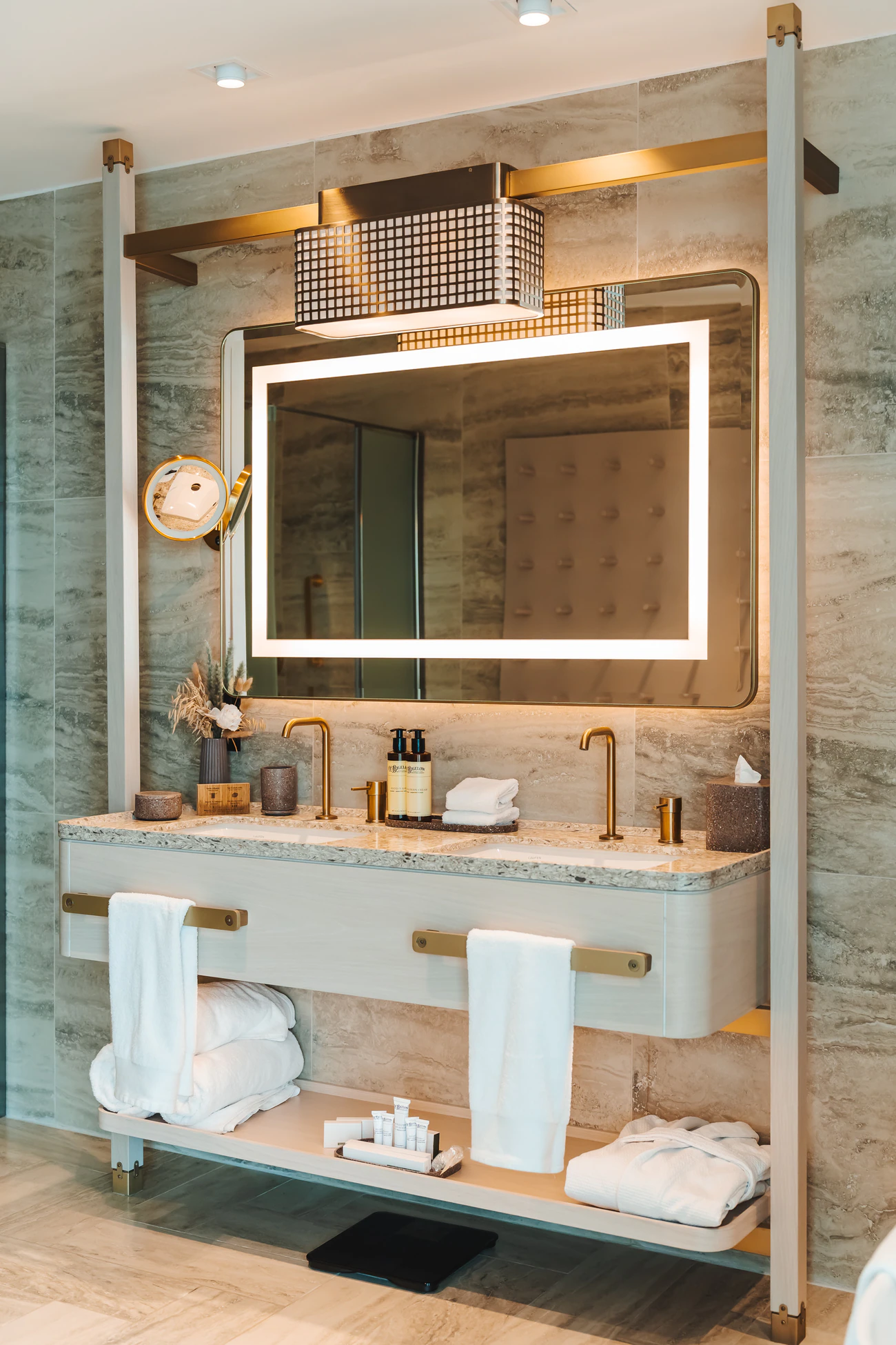 Vanity with an illuminated mirror and shelves of towels in pale marble.