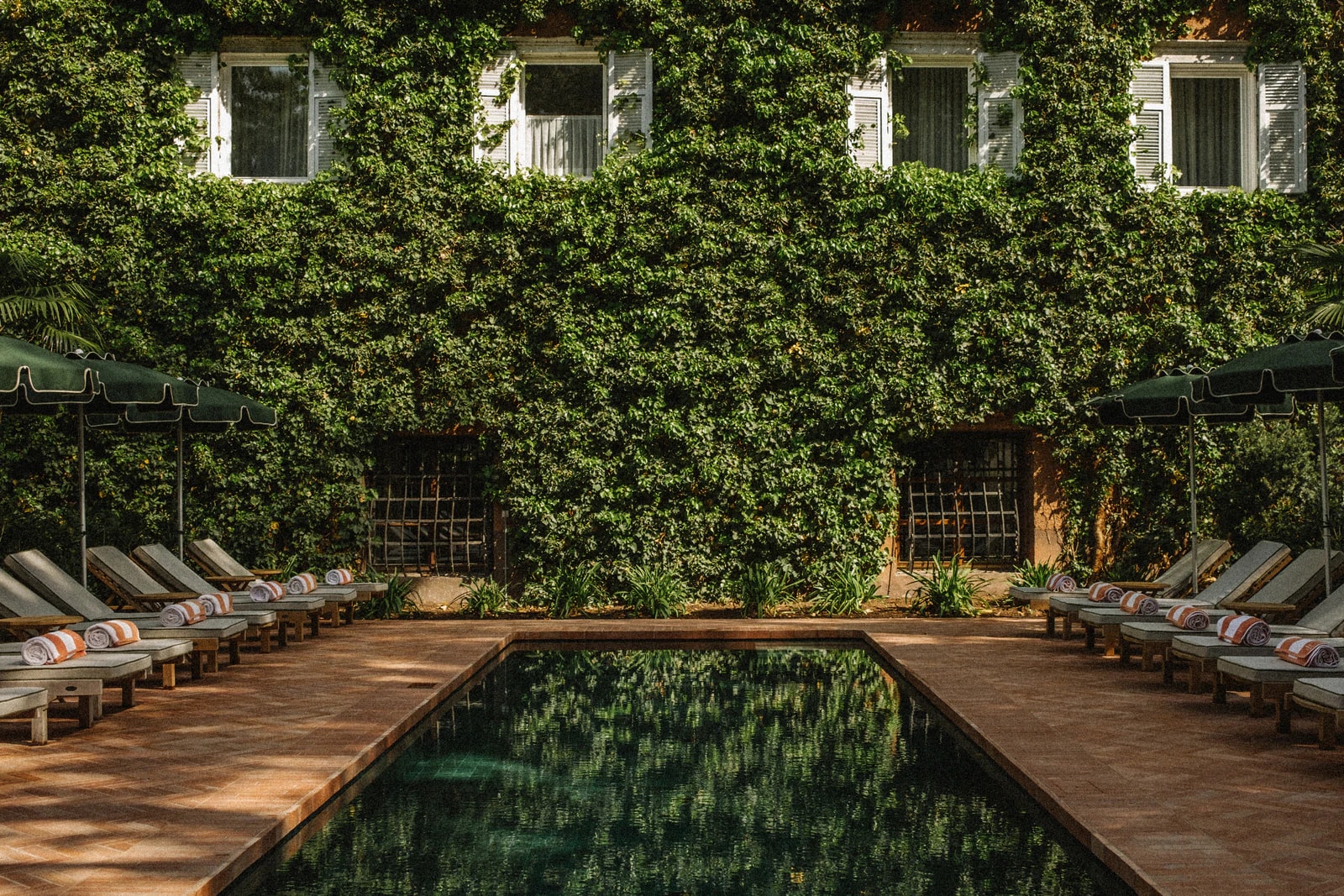 Efeubewachsene Fassade des Parkhotel Mondschein mit Pool und Liegen im Park