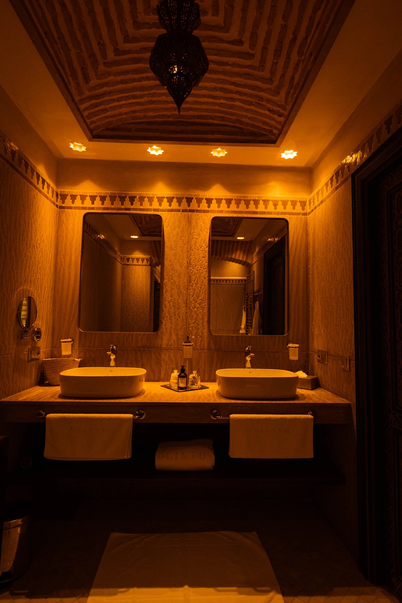 Badezimmer mit zwei Aufsatzwaschbecken, Spiegeln und gewölbter Backsteindecke im warmen Licht.