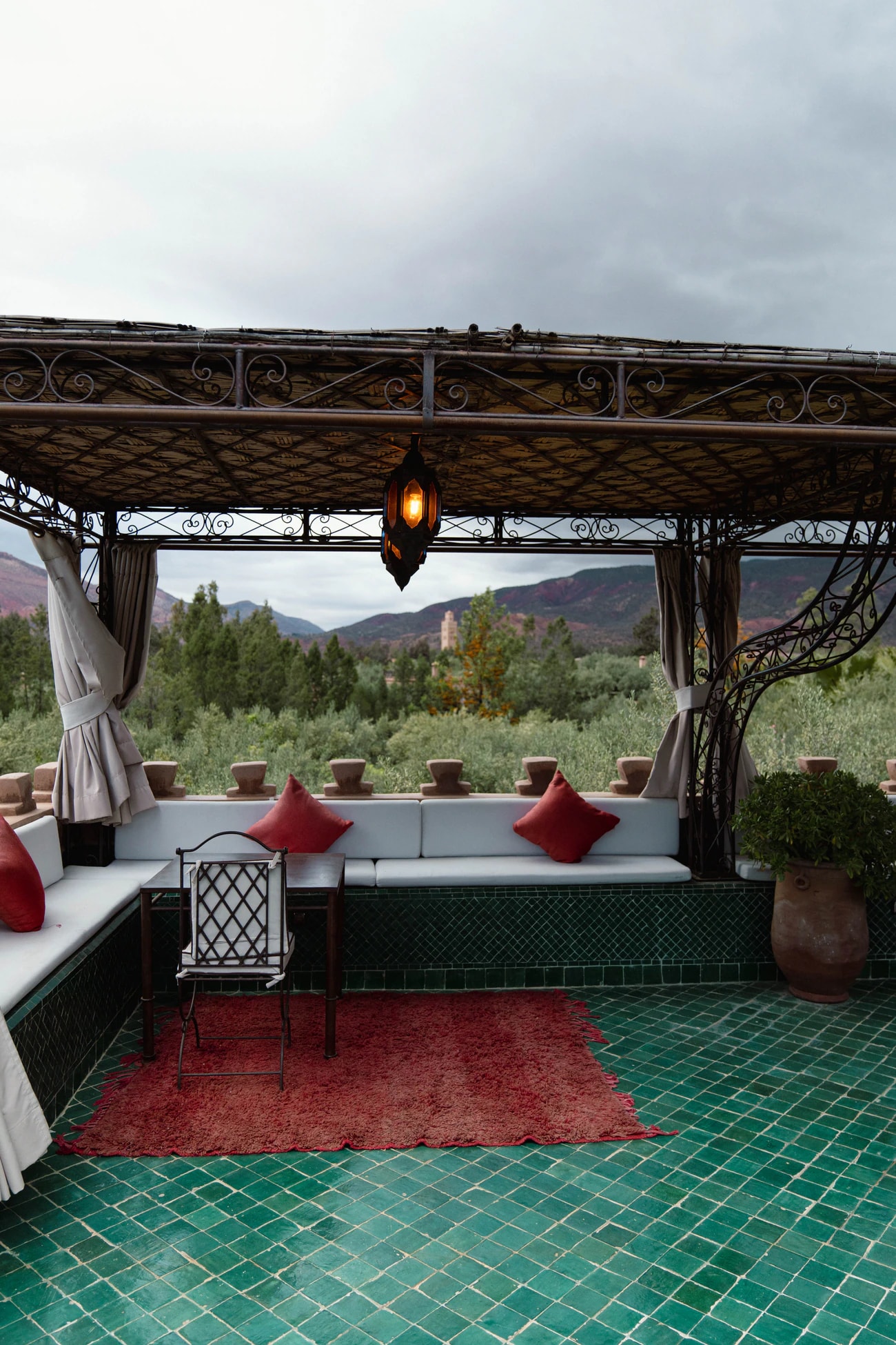 Dachterrasse mit grünen Fliesen, Polsterbank unter einer Pergola und Blick auf Olivenhaine und Berge.