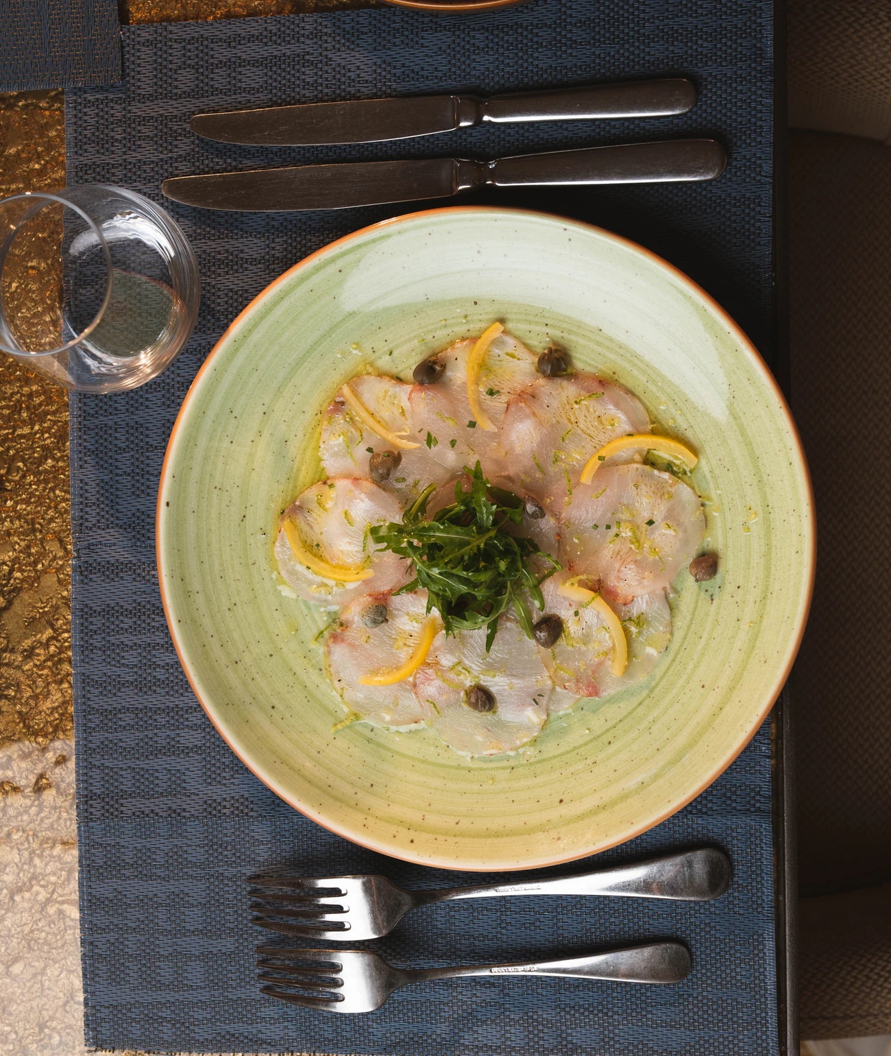 Carpaccio mit Zitrone, Kapern und Kräutern auf einem grünen Teller, von oben fotografiert.