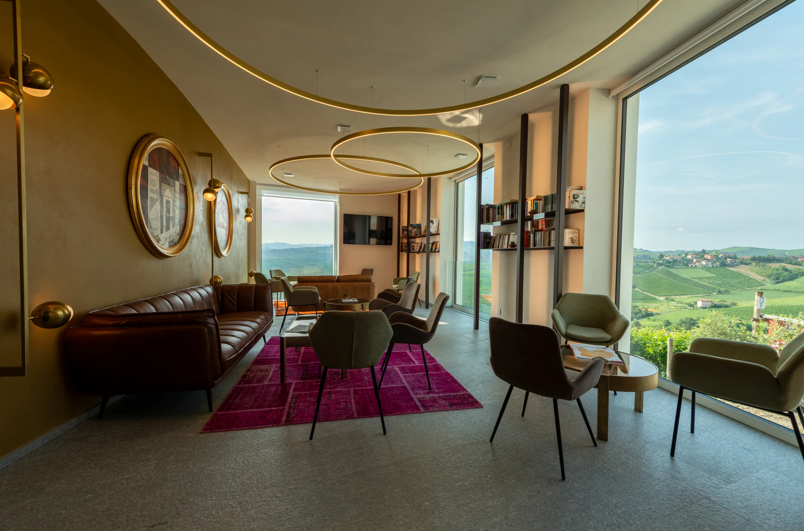Lounge mit Ledersofas, rotem Teppich und runden Spiegeln, durch das große Fenster die Reben.