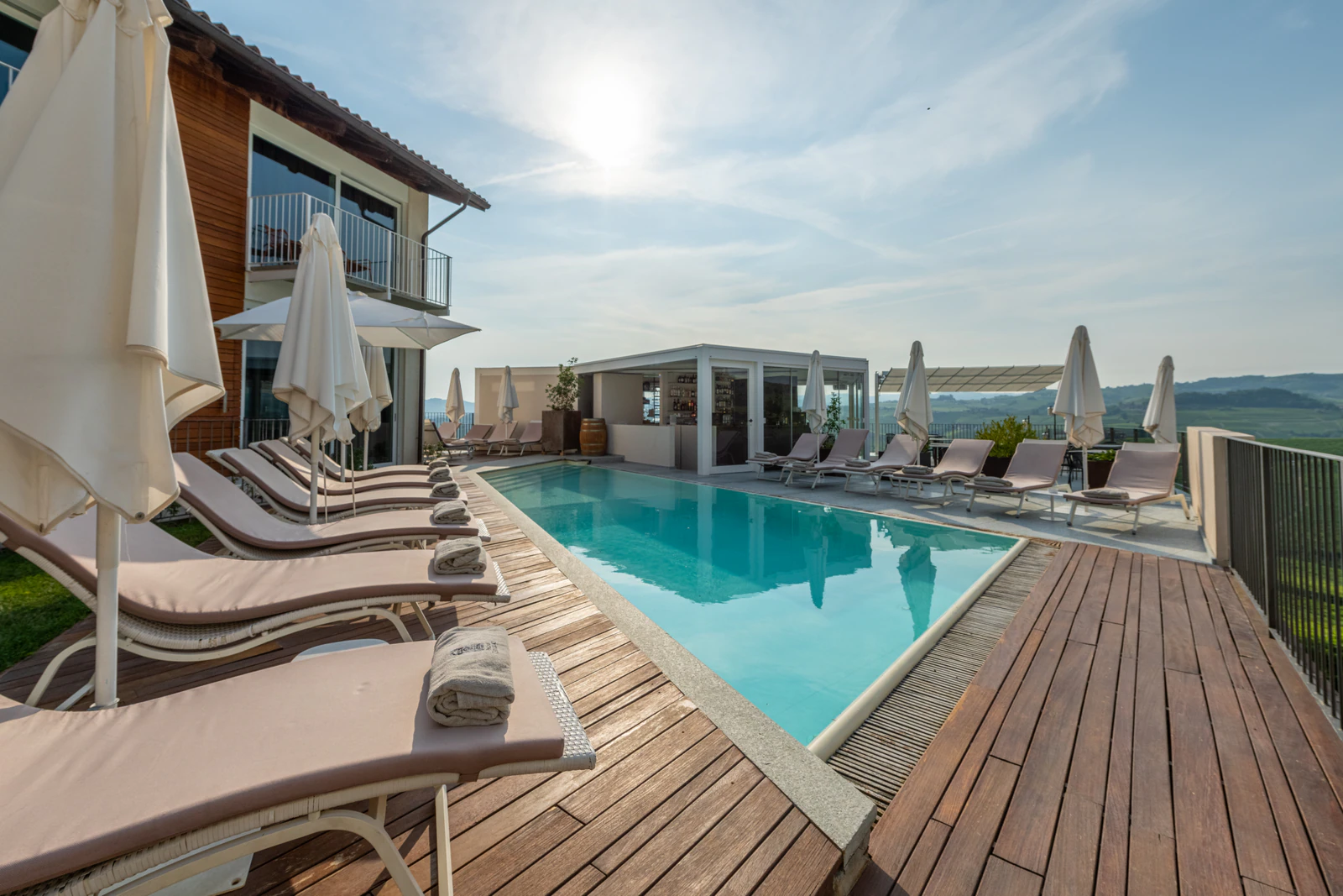 Infinity-Pool mit Holzdeck und Liegen über den Hügeln der Langhe.