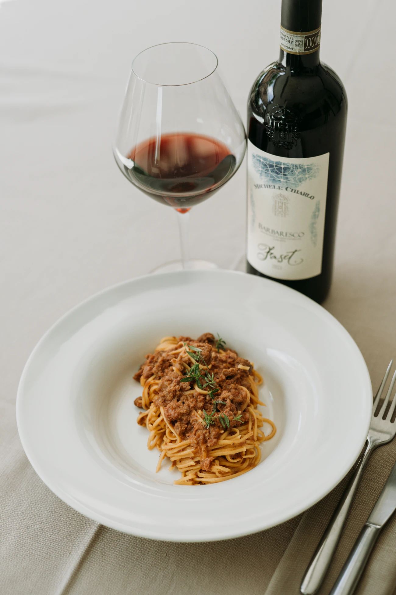 Feine Bandnudeln mit Ragù, daneben ein Glas Rotwein und eine Flasche.