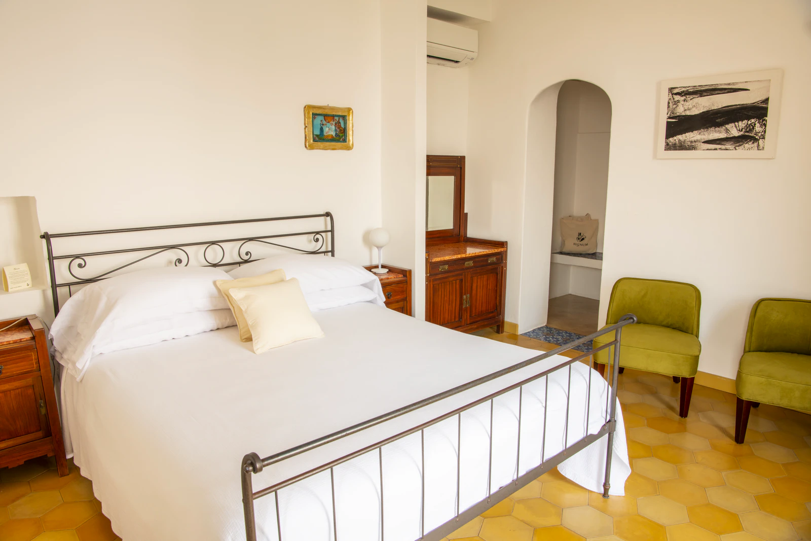 Deluxe-Zimmer mit schmiedeeisernem Bett und zwei grünen Sesseln.
