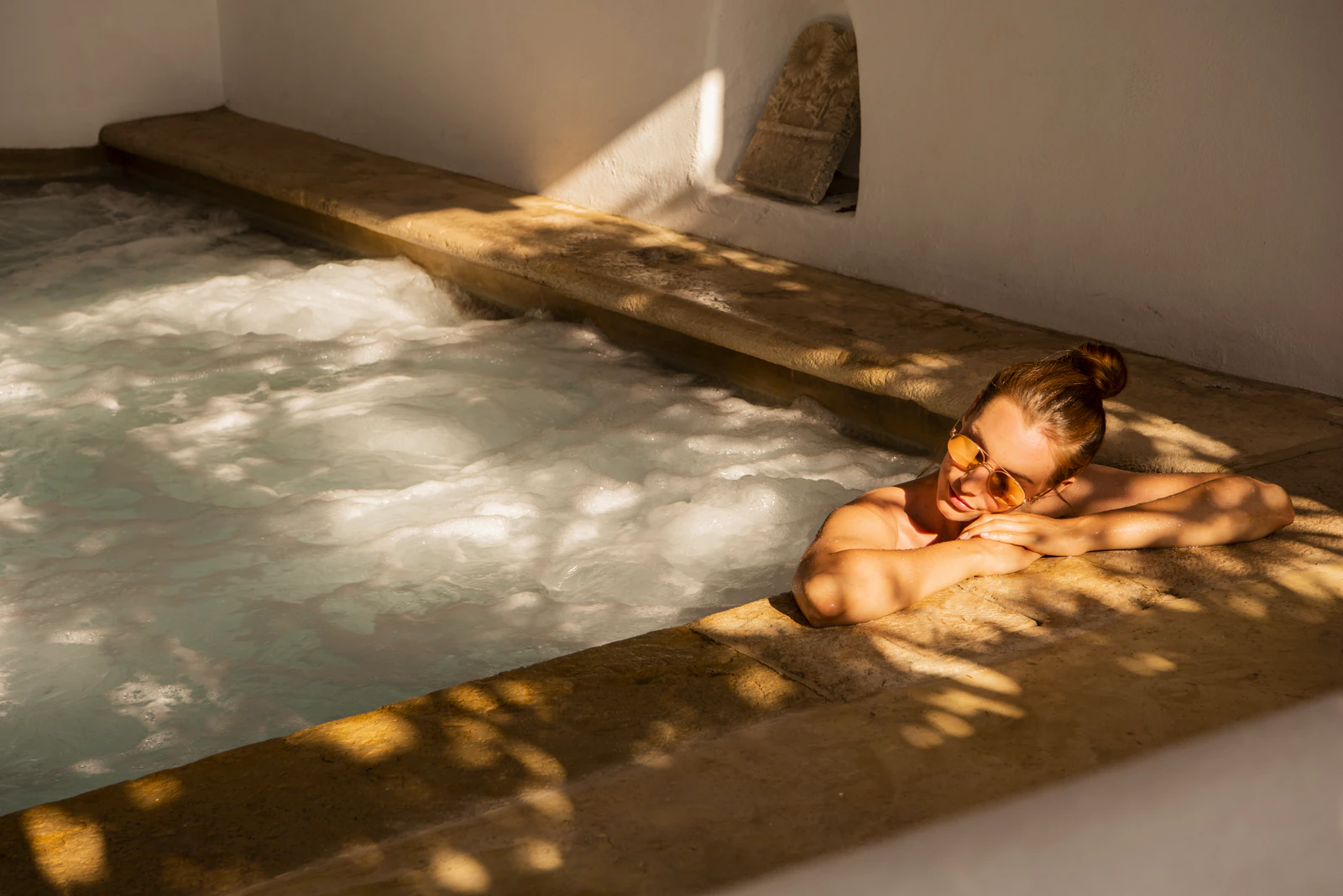 Frau im Whirlpool aus Stein im Sonnenlicht.