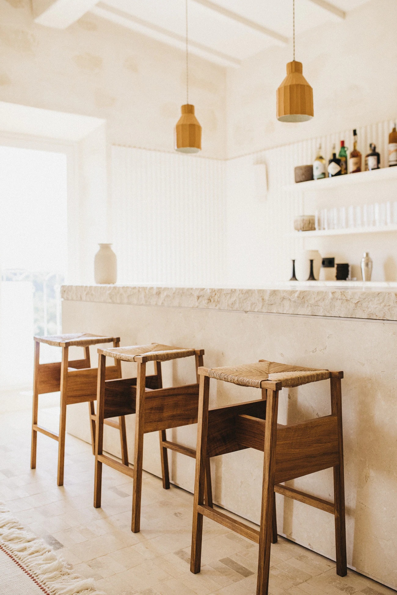 Helle Bar mit Holzhockern und Flaschen im offenen Wandregal.