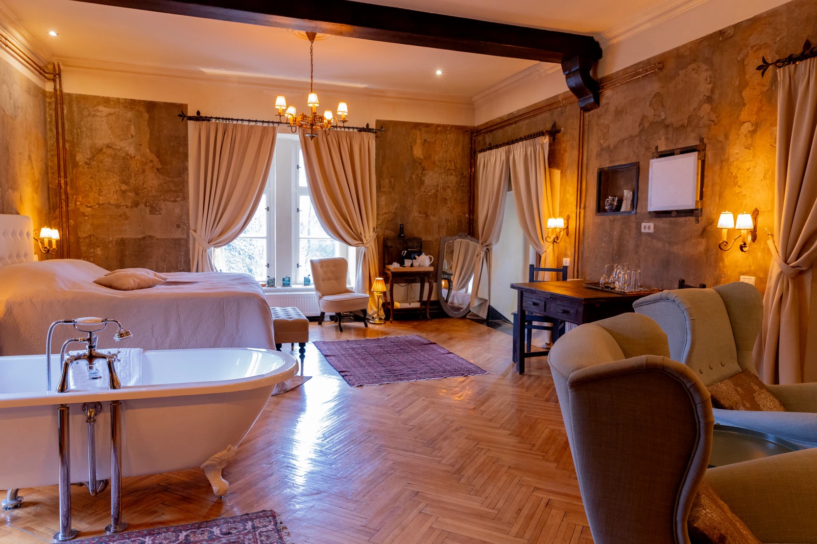 Zimmer im Herrenhaus mit freistehender Badewanne, Bett, Sesseln und Kronleuchter.