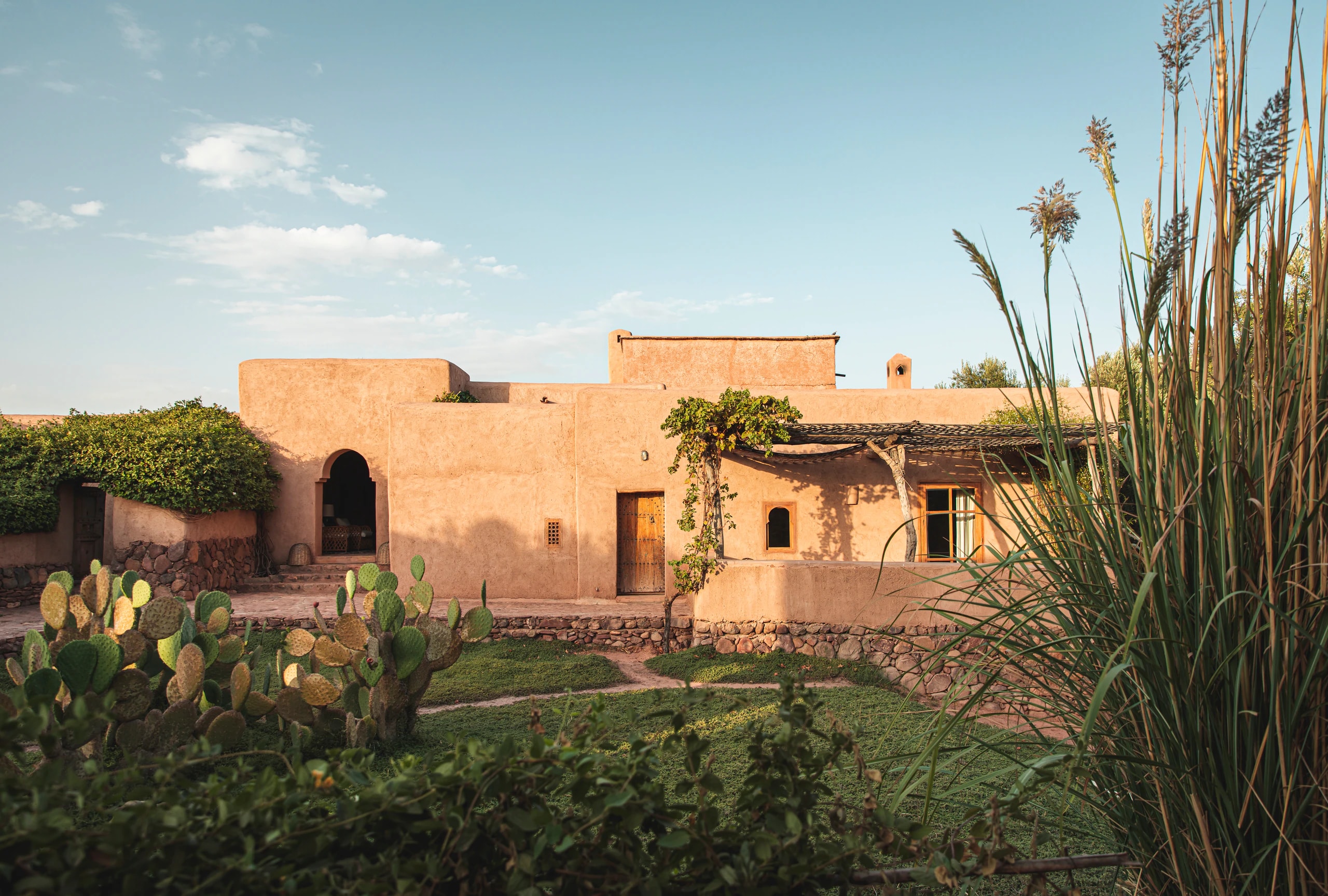 Lehmbauten der Berber Lodge mit Garten, Kakteen und Gräsern im Abendlicht