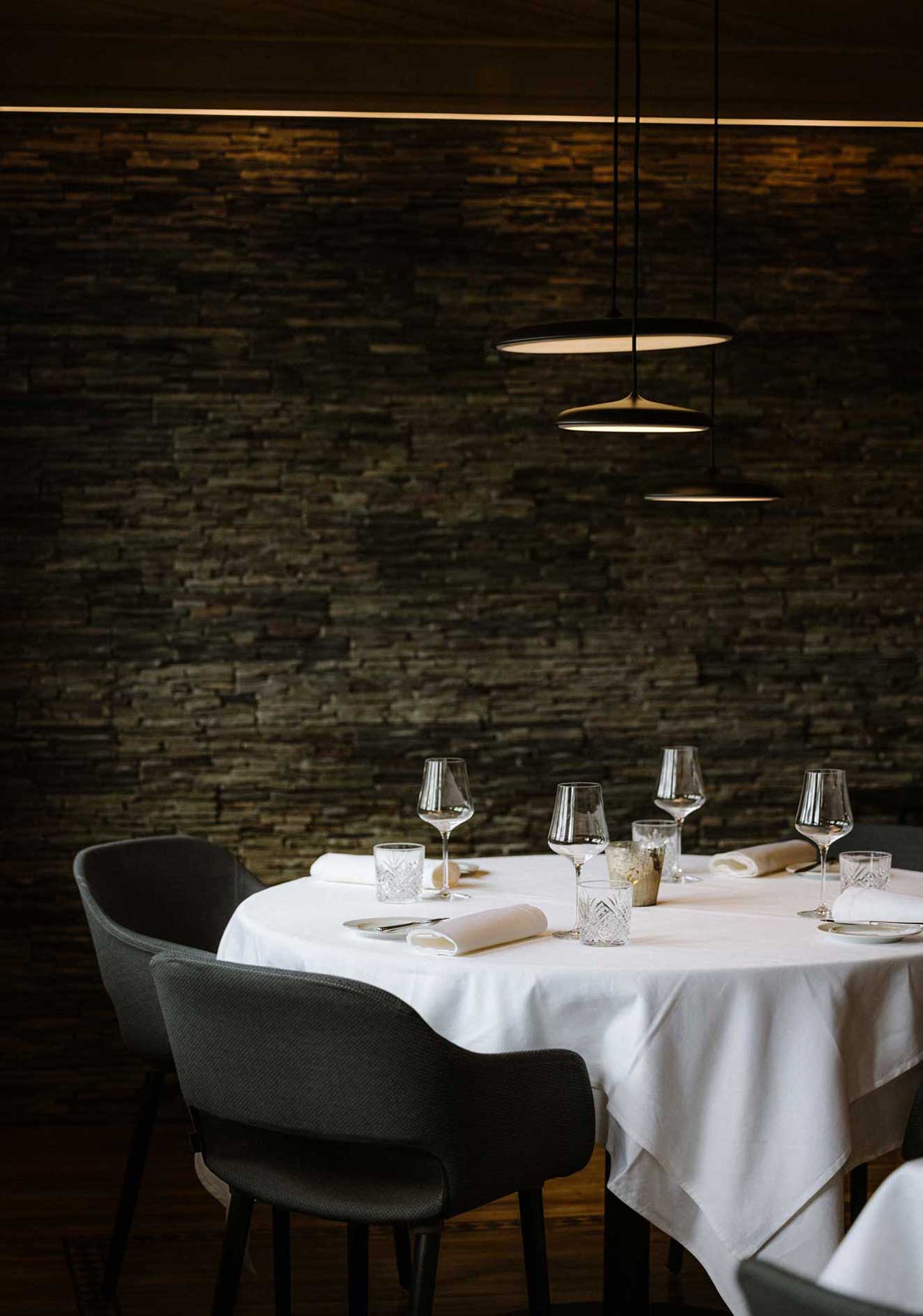 Stuba Adelboden — Dining room with stone wall and pendant lamps, Restaurant Alpenblick