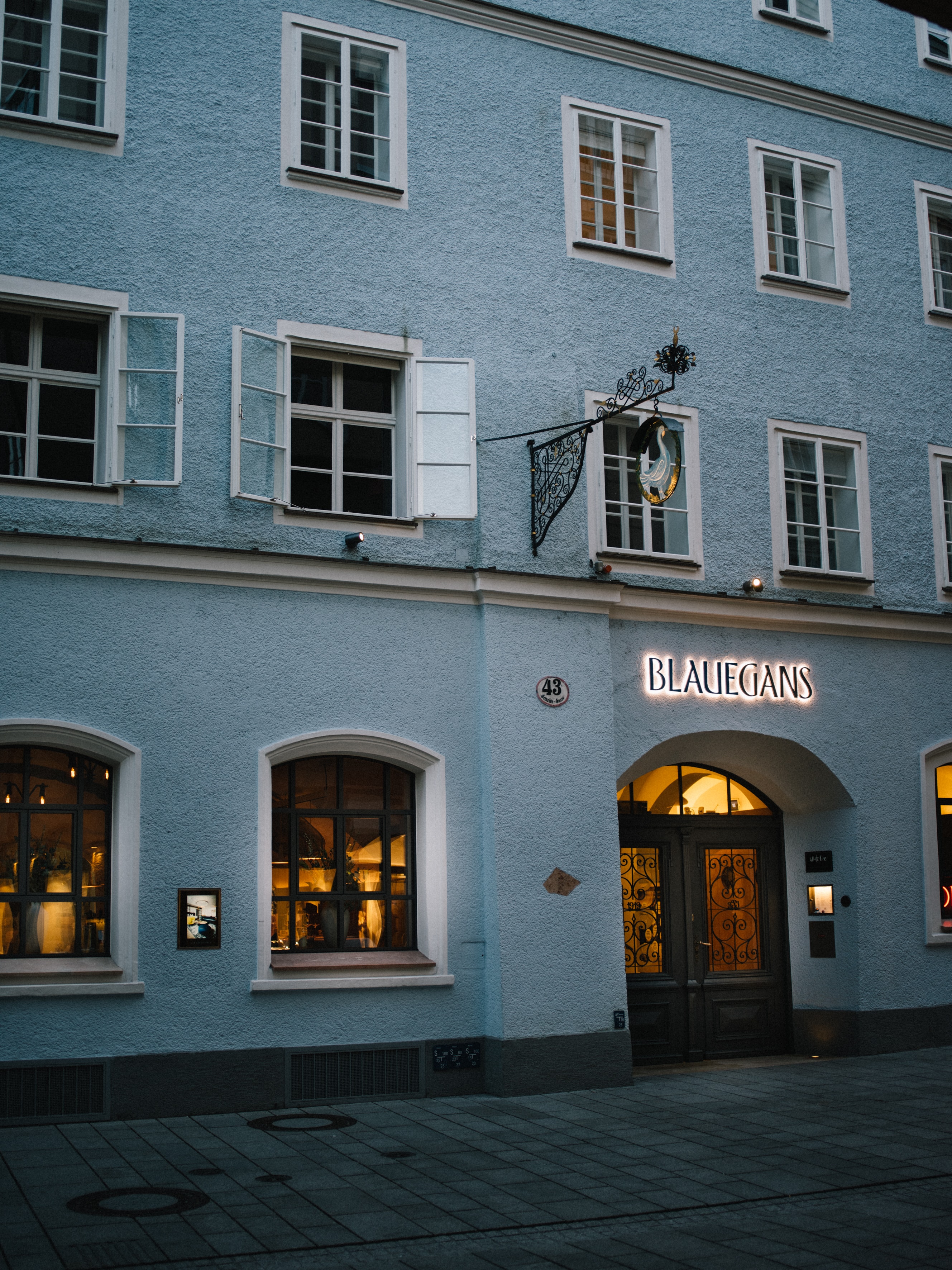 Arthotel Blaue Gans — blaue Barockfassade in der Getreidegasse mit beleuchtetem Schriftzug und schmiedeeisernem Gänse-Zunftschild bei Dämmerung