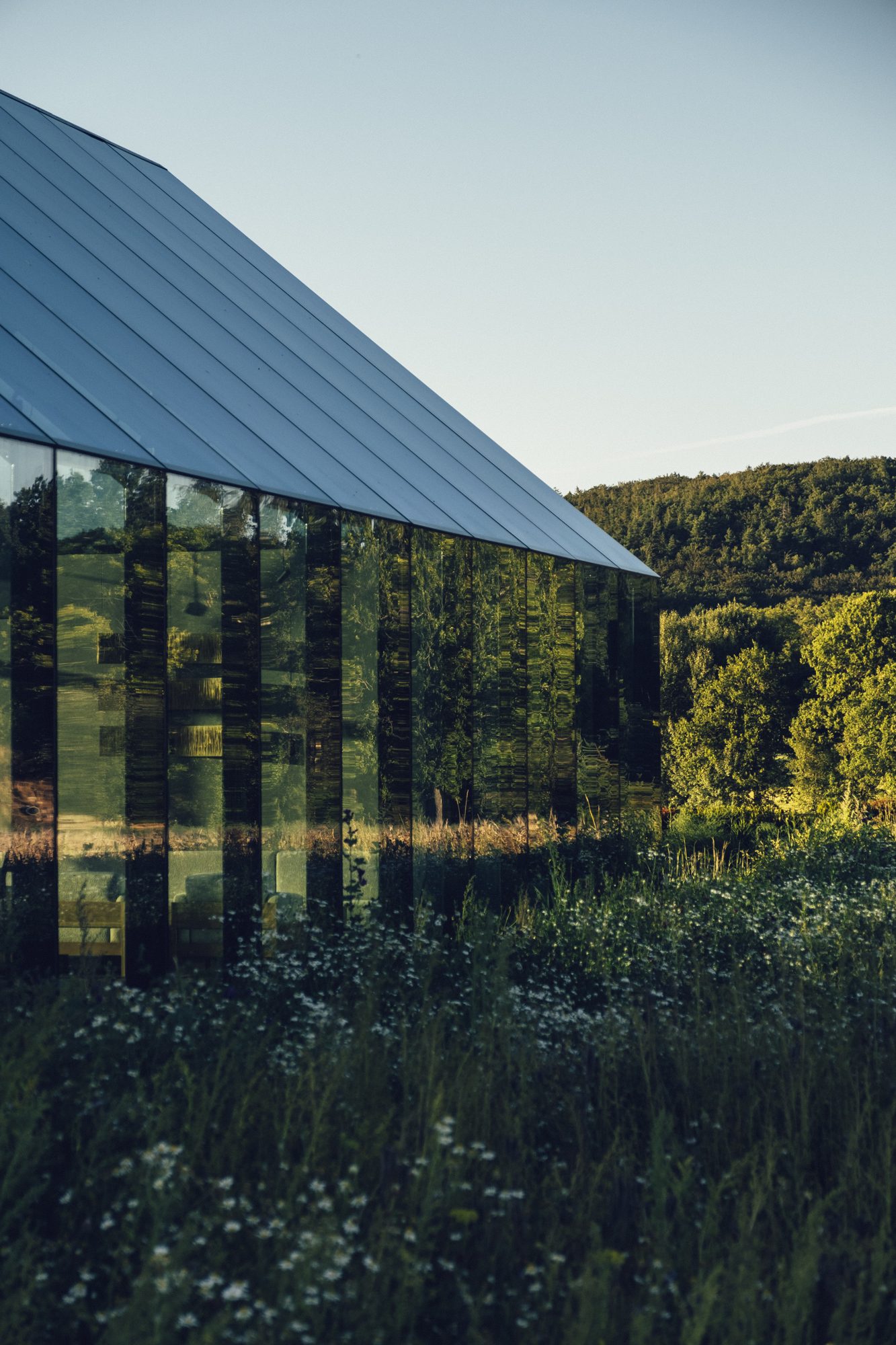 Restaurang ÄNG, Ästad Vingård — die geneigte Glasfront des Restaurants spiegelt die umgebende Natur