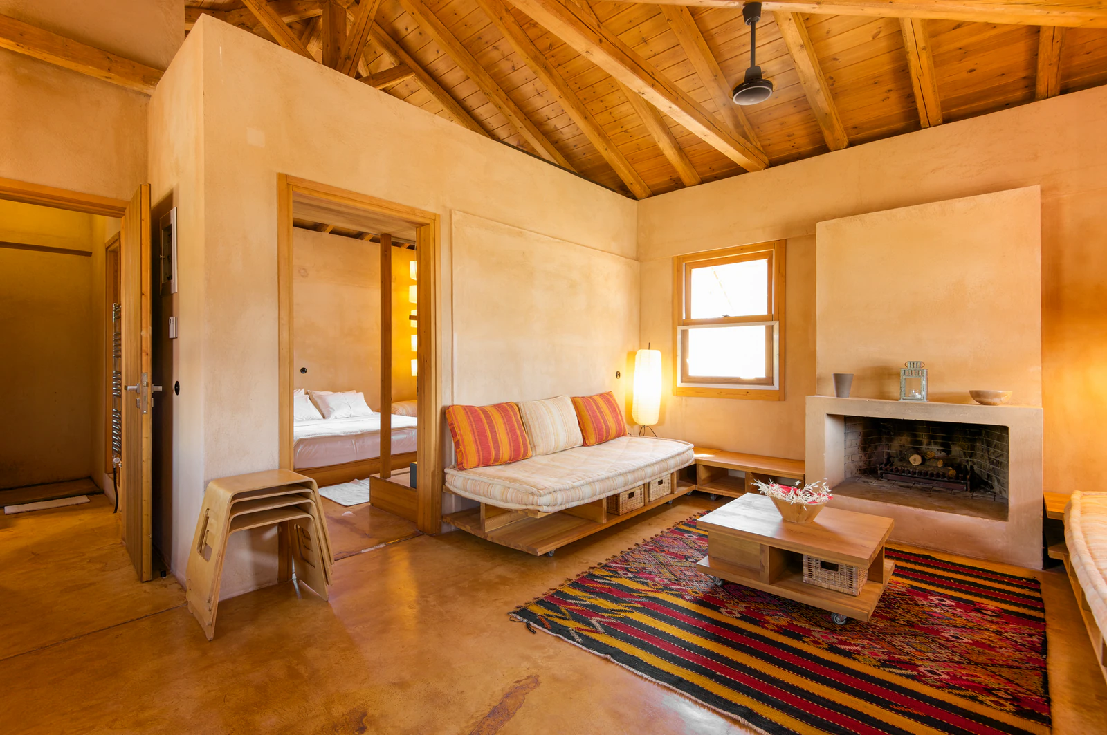 Living room of a guest house with a timber ceiling, fireplace, sofa and rug. Photo: Eumelia