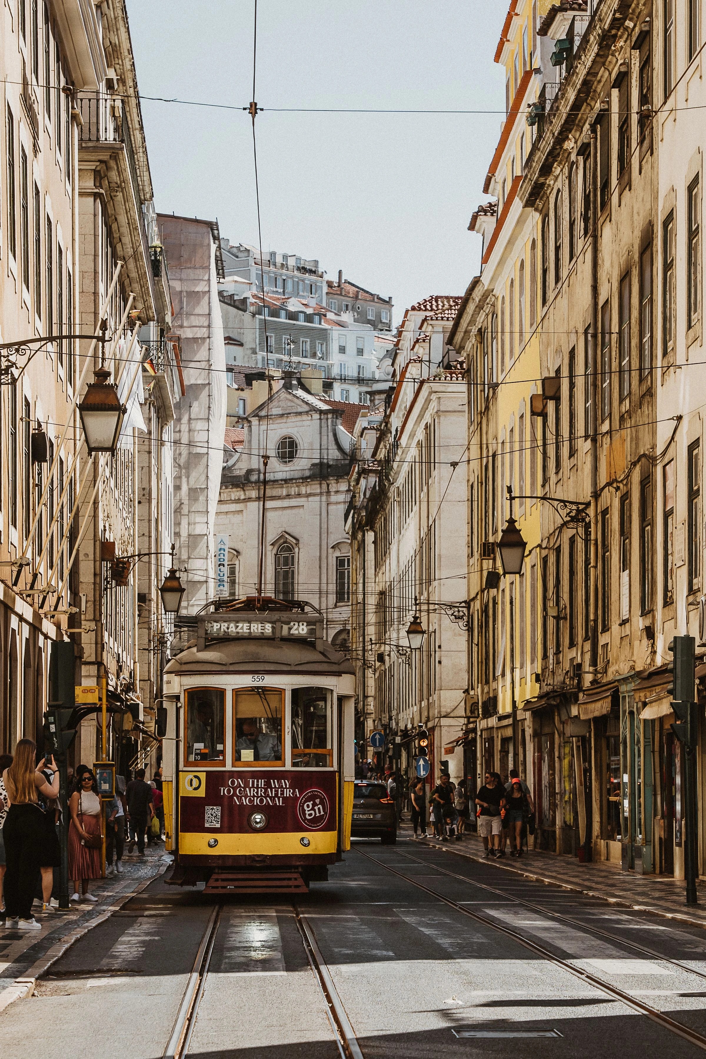Symbolbild: gelbe Straßenbahn in einer engen Straße der Lissabonner Innenstadt. Foto: Masood Aslami / Pexels