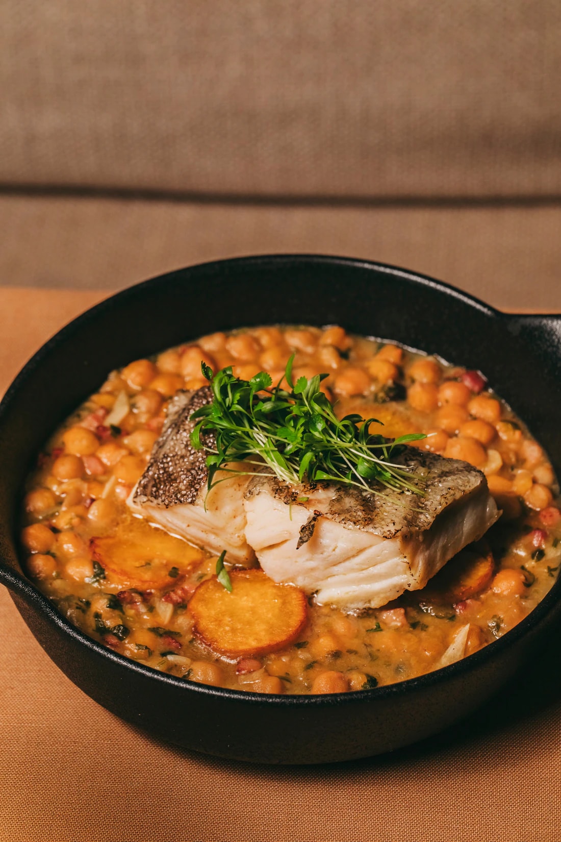 Roast cod on chickpeas with slices of sweet potato in a black pan